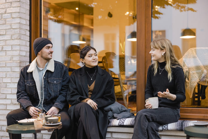 Drei Freunde sitzen vor einem Straßencafé und unterhalten sich, während sie einen Kaffee trinken.