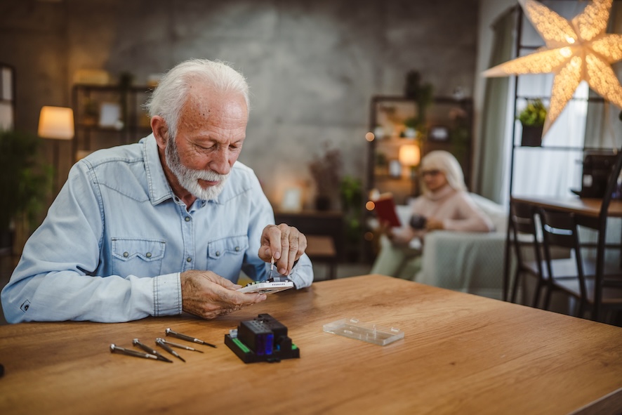 Älterer Herr am Tisch bei der Reparatur eines elektronischen Gerätes